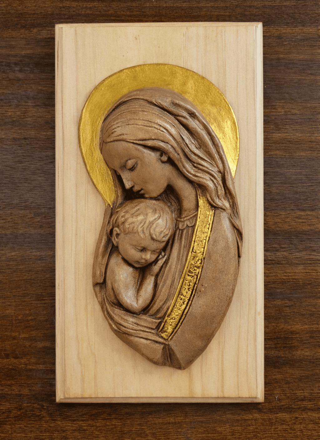 Relieve de la Virgen con el Niño dormido sobre su pecho, montado en tabla de pino claro con halo en pan de oro.